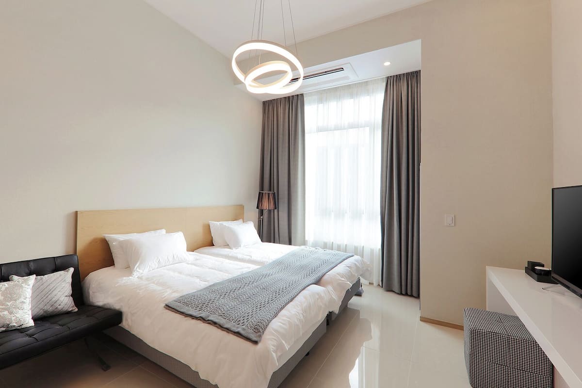 Ein modernes Hotelzimmer mit Bett, einer Couch, einem Fernseher und einem großen Fenster mit Vorhängen.