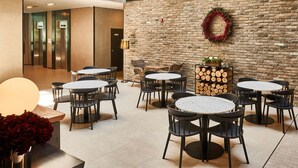 A lobby with round tables and chairs, a brick wall with a wreath, and a stack of firewood. - Withland Hotel Pyeongchang (Pyeongchang)