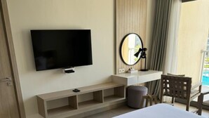 Ein Hotelzimmer mit einem großen Bett, einem an der Wand montierten Fernseher, einem Schreibtisch mit Stuhl und einem Fenster mit Vorhängen.