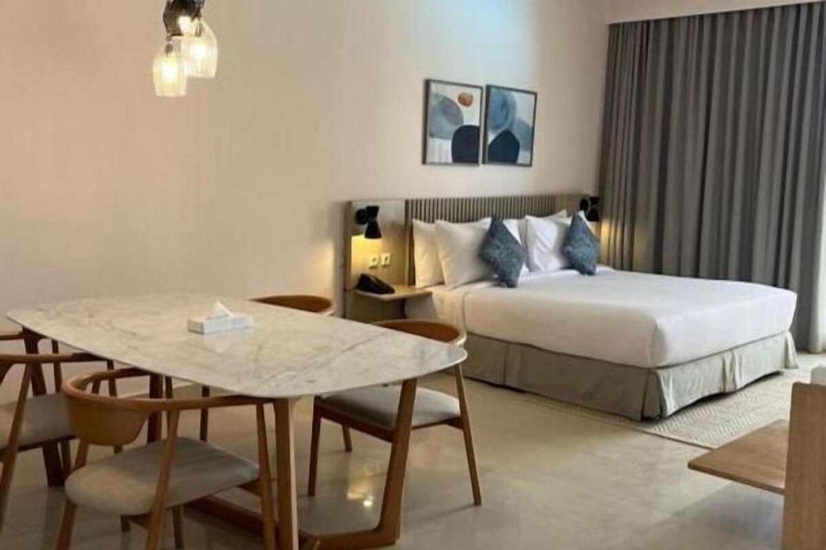 Een hotelkamer met een bed, een eettafel met stoelen, een nachtkastje met lamp en kunst aan de muur.