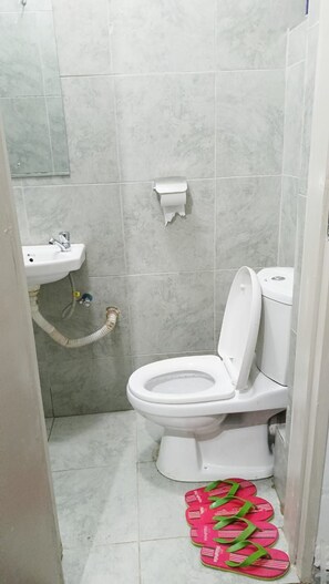 A small bathroom with a toilet, sink, and a toilet paper holder. - Lux Suites Tsavo Sunset Apartments  (Nairobi)