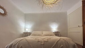 Un dormitorio con cama, dos mesitas de noche, una puerta y un adorno en la pared.