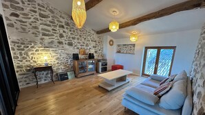 Amplia sala de estar con pared de piedra, vigas de madera, un sofá azul claro y un mueble de madera.