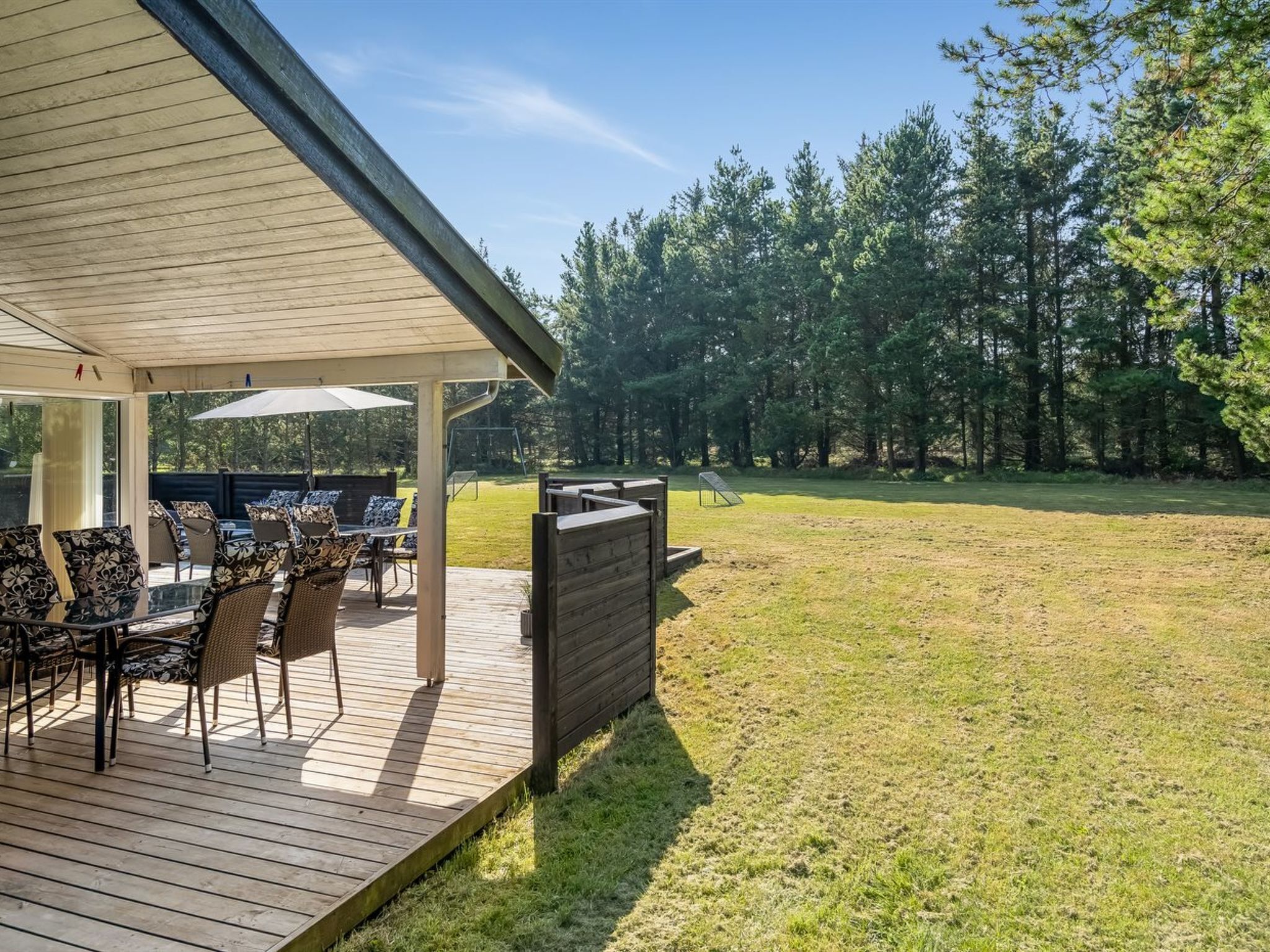 Un patio couvert, aménagé avec du mobilier d’extérieur, donnant sur un espace verdoyant avec des arbres.