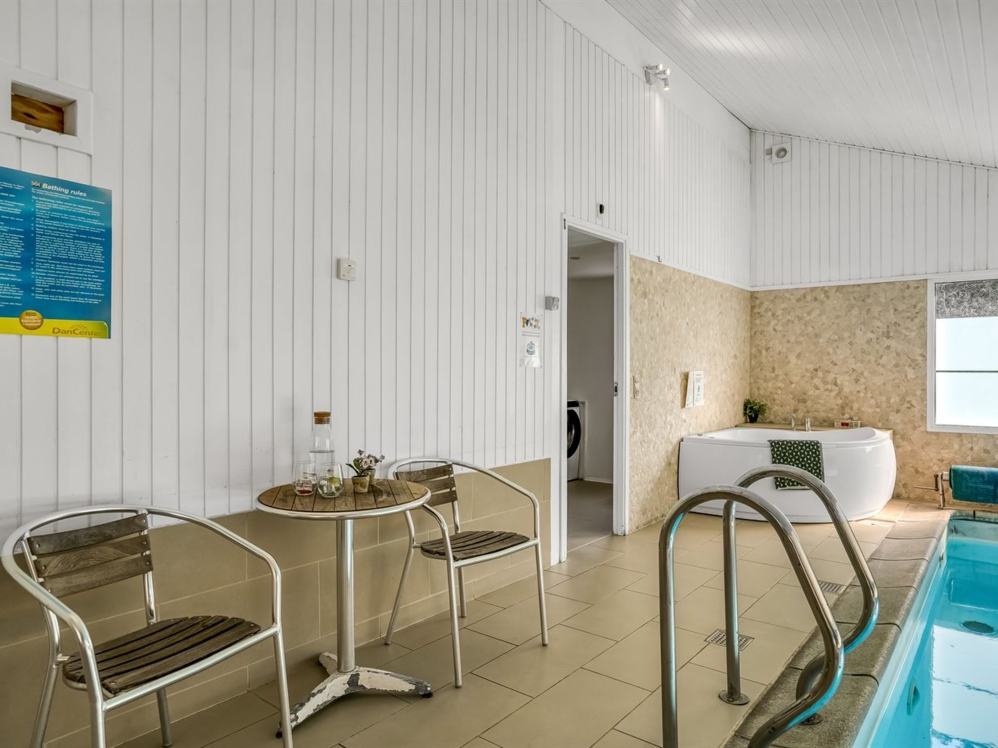 Une salle de bain propre et moderne, dotée d’une baignoire, d’un espace douche et d’un petit coin salon avec des chaises et une table.