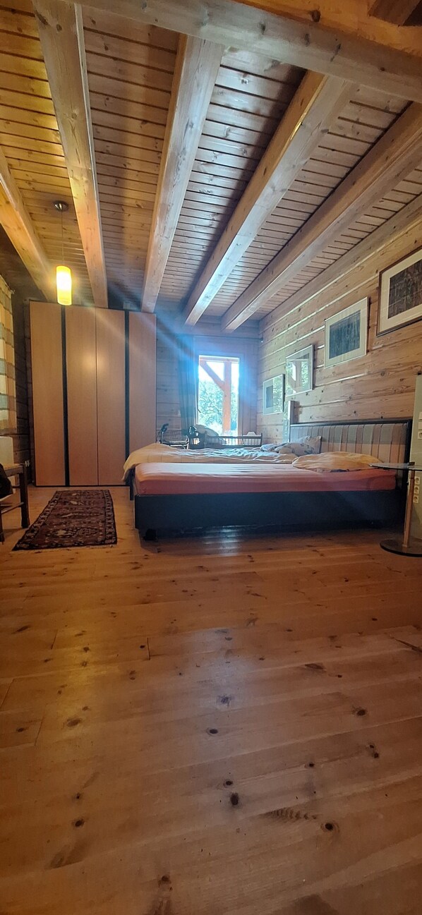 Une chambre dans une cabane en bois, avec un lit, une commode et une grande fenêtre.