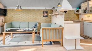 Un espacio habitable compacto con sofá, una pequeña mesa de madera, una zona de cocina con microondas y un colgante.