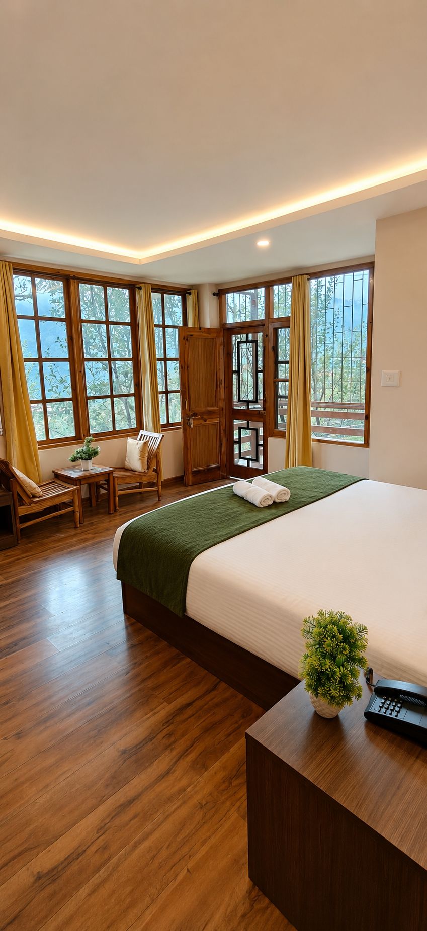Una habitación de hotel con una cama grande, muebles de madera, un escritorio y vistas a árboles por las ventanas.