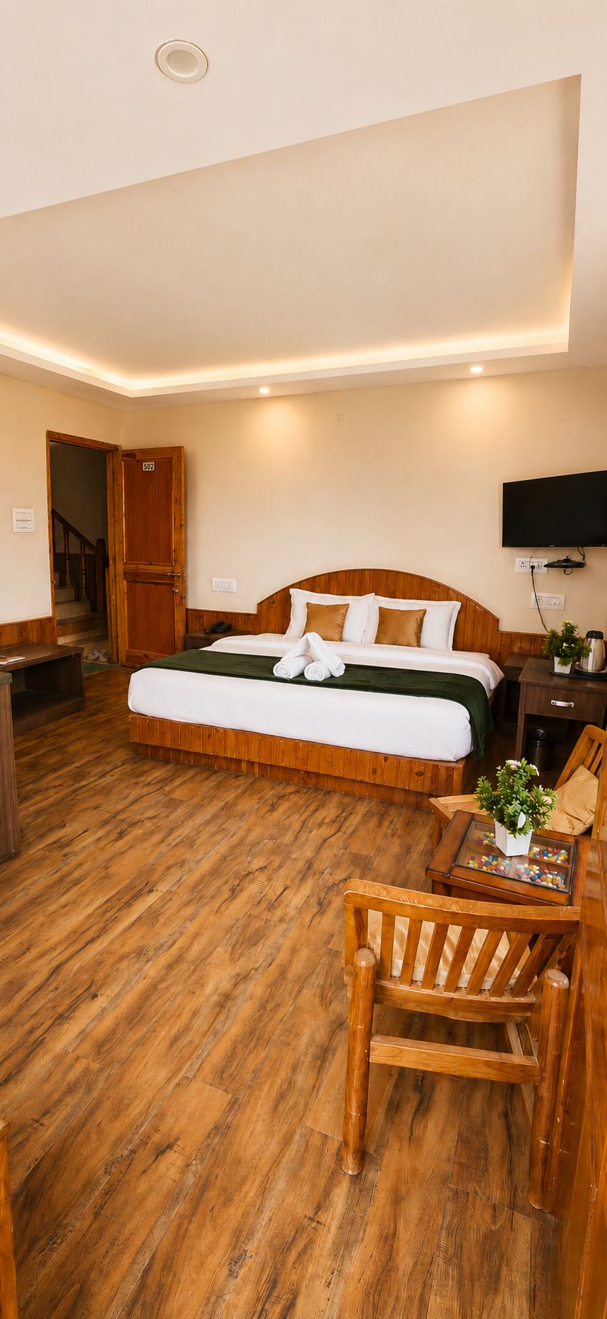 A hotel room with a large bed, wooden flooring, a television, and a small table with a plant.
