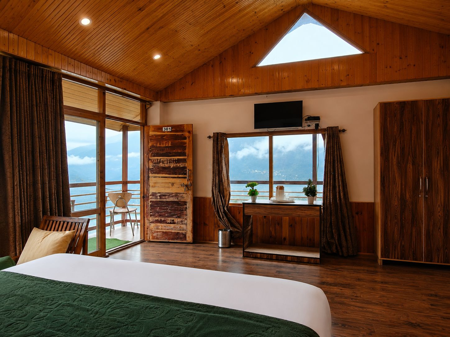 Una habitación con cama, escritorio, silla, televisor y un amplio ventanal con vista al mar.
