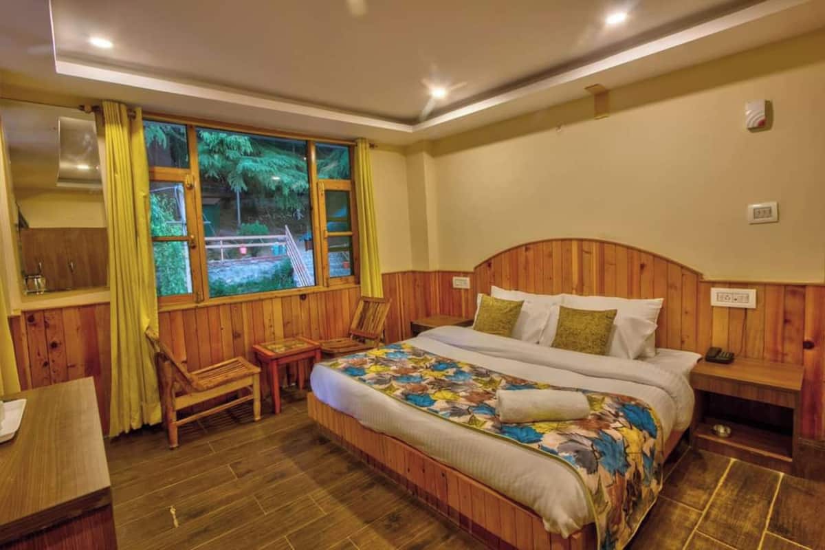 A wooden-paneled bedroom with a large bed, a small table, two chairs, and a window with curtains.