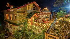 A multi-story building with a stone facade, wooden balconies, and a well-lit exterior. - Mahamaya Resort (Manali)