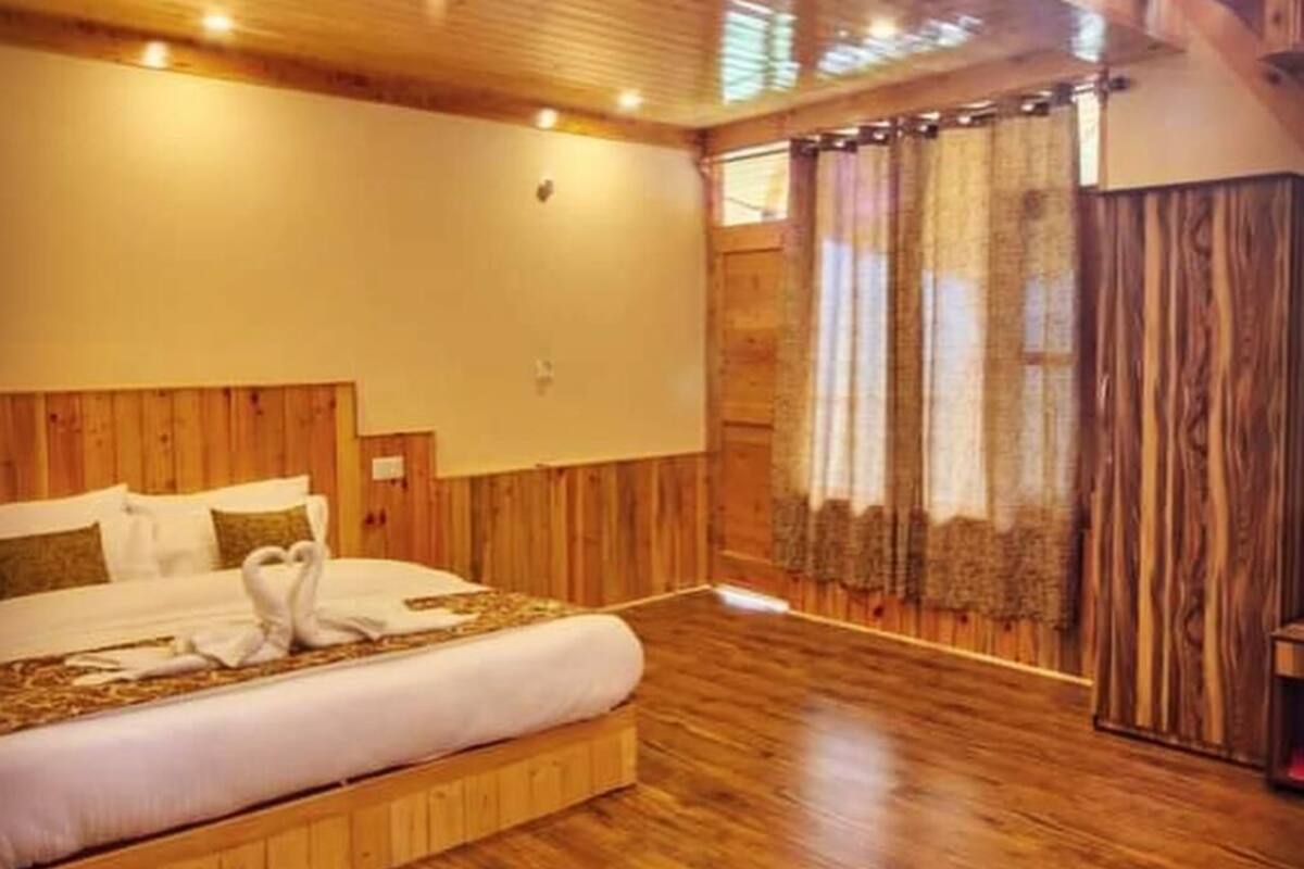 A wooden-floored bedroom with a large bed, a wooden ceiling, and a view of the outdoors.