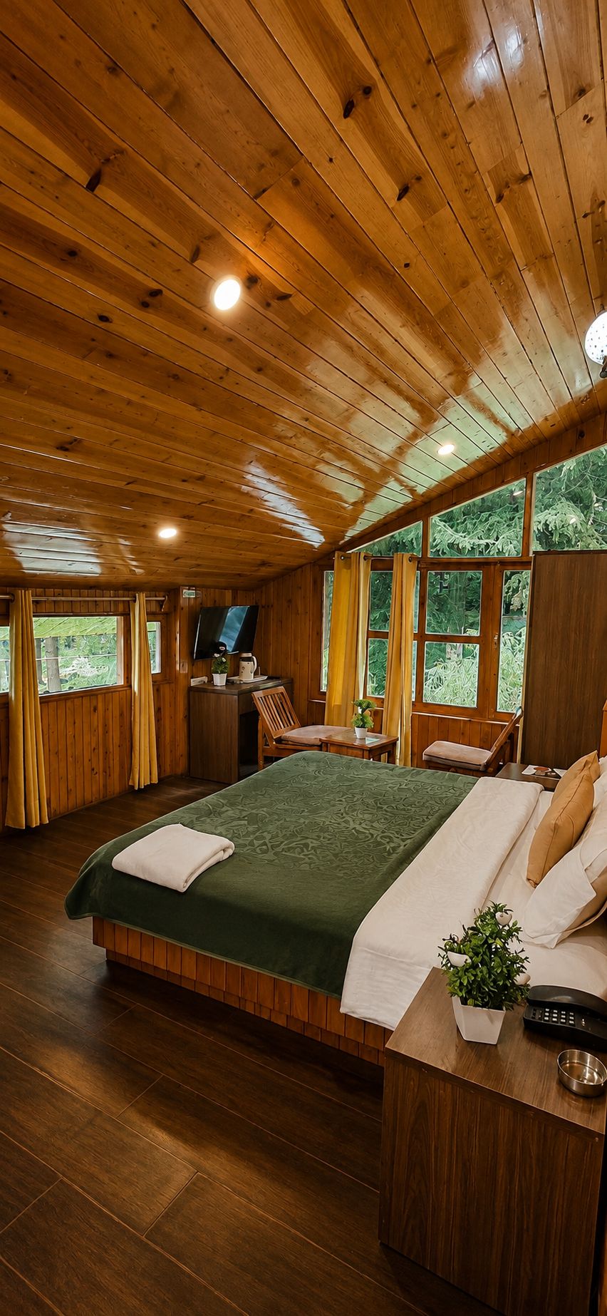 A wooden cabin bedroom with a large bed, a desk with a chair, a television, and a window with curtains.