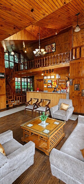 A spacious lobby with a high ceiling, wooden walls, a reception desk, and a staircase leading to an upper level.