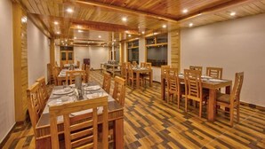 A dining area with wooden tables and chairs, a checkered floor, and a high wooden ceiling with recessed lighting. - Mahamaya Resort (Manali)