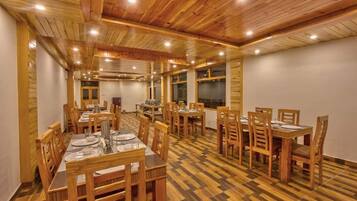 Un espace repas avec des tables et des chaises en bois, un sol à carreaux et un haut plafond en bois doté d’un éclairage encastré.