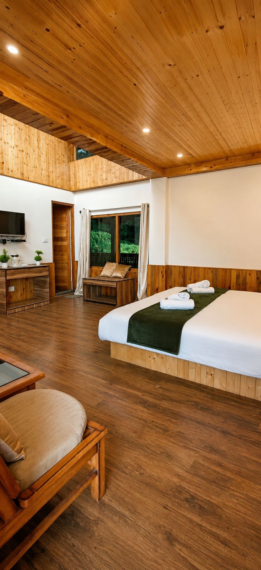 Une chambre d’hôtel avec un plancher en bois, un lit, un bureau, une télévision et une fenêtre avec des rideaux.