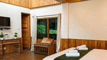 Une chambre d’hôtel avec un plancher en bois, un lit, un bureau, une télévision et une fenêtre avec des rideaux.