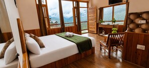 A room with a bed, a desk, and a chair, with a view of mountains through large windows.