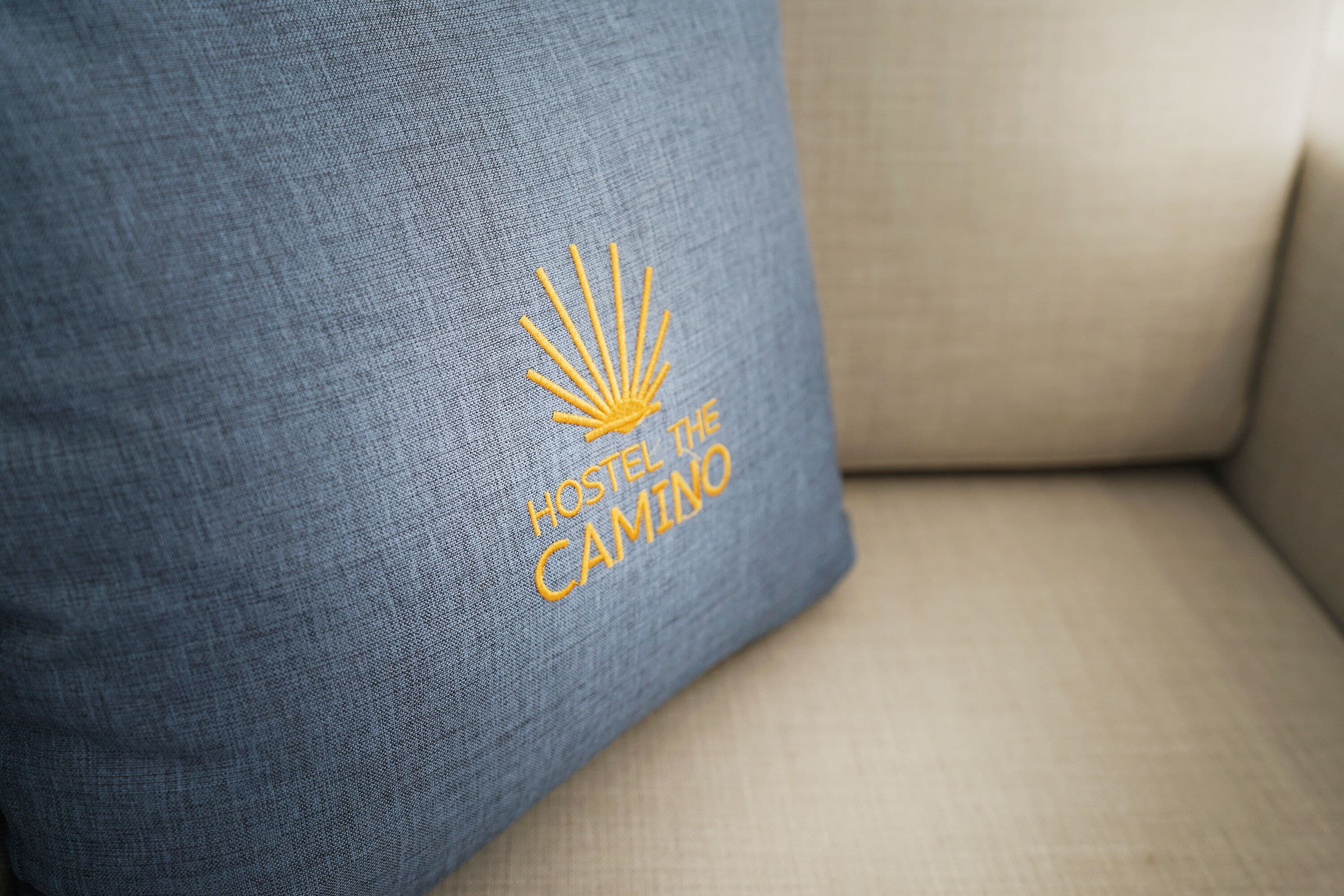 A blue pillow with embroidered text and a sun-like design.