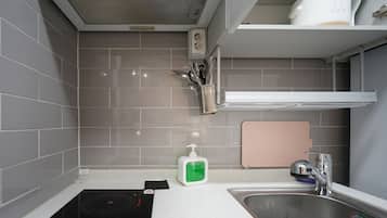 Een moderne keuken met grijze tegels, een ingebouwde kookplaat, een spoelbak en een plank met keukengerei.