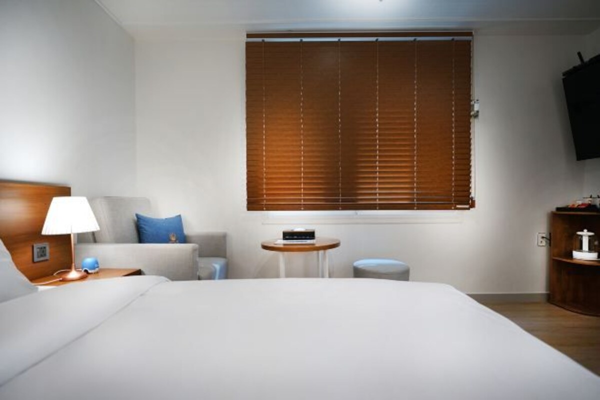 Een hotelkamer met een bed, nachtkastje, lamp en een klein rond tafeltje.