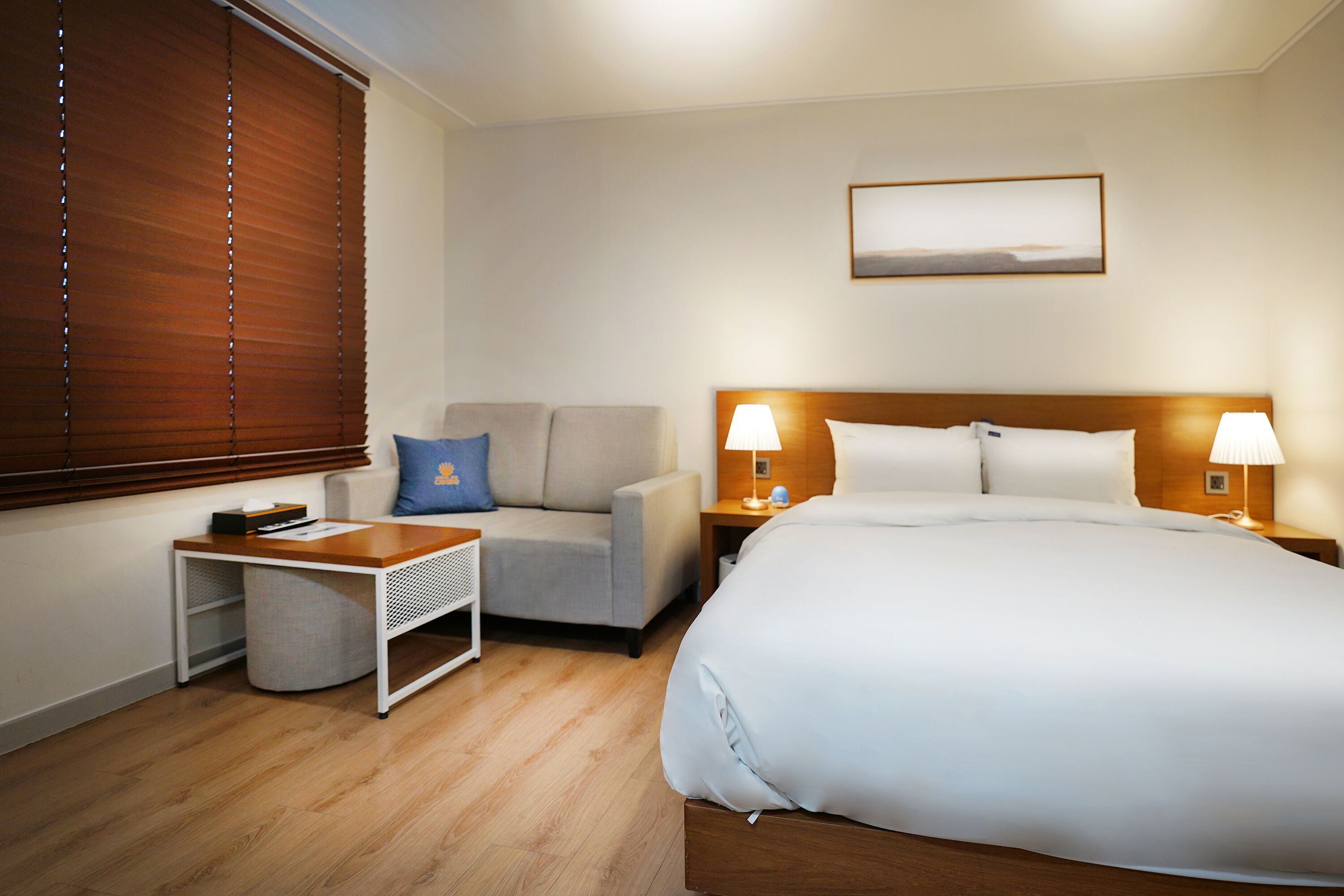 A hotel room with a bed, a sofa, a small table, and a nightstand with lamps.
