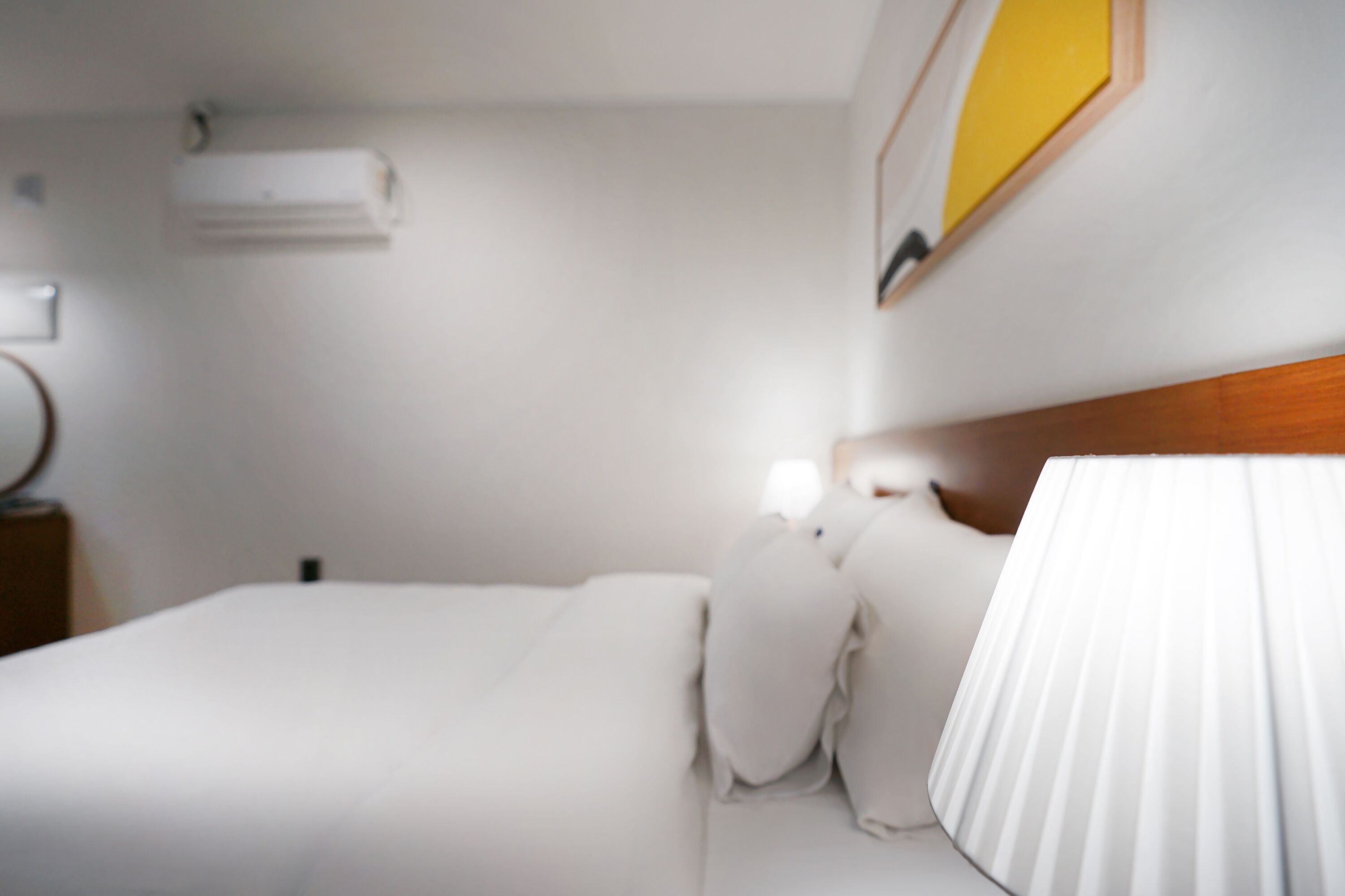Une chambre d’hôtel comprenant un lit, une table de chevet, une lampe et un climatiseur fixé au mur.