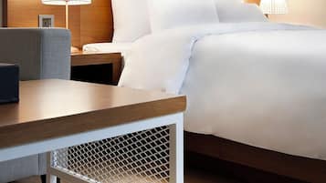A hotel room with a large bed, two bedside tables with lamps, a wooden headboard, a small desk, and a wall-mounted picture.
