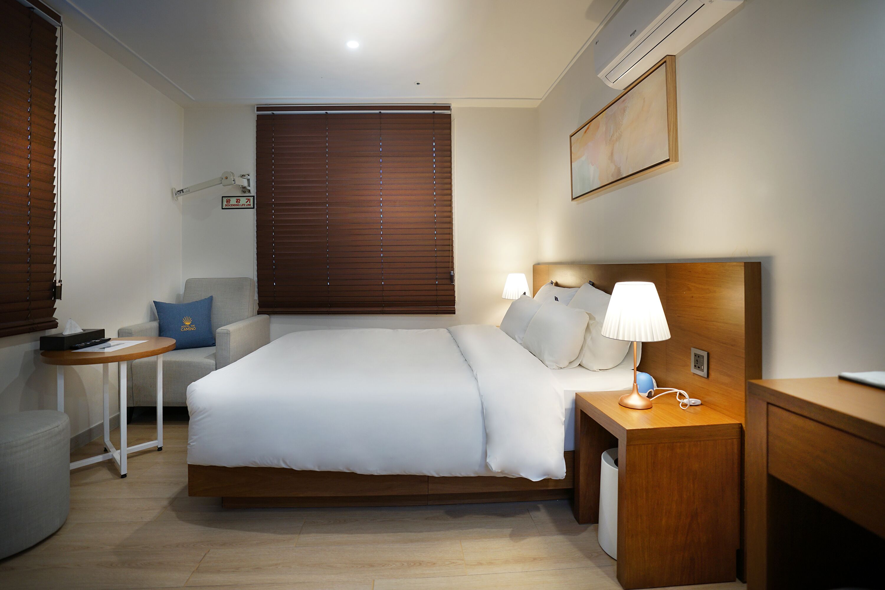 A hotel room with a bed, bedside table, lamp, and a small table with a remote control.