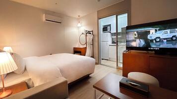 Habitación de hotel con cama, mesita de noche, lámpara, televisor y puerta corredera que da a una zona de cocina.