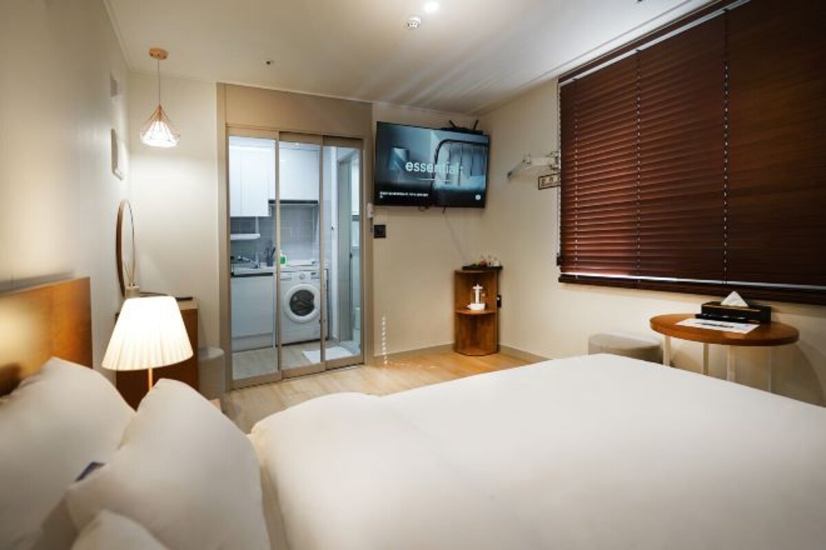 Habitación de hotel con cama, televisión, lavadora y una mesita.