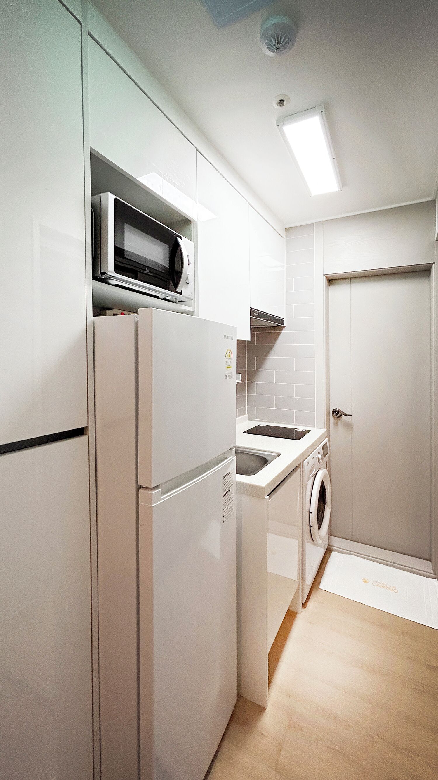 A compact kitchen with a microwave, refrigerator, sink, and washing machine.