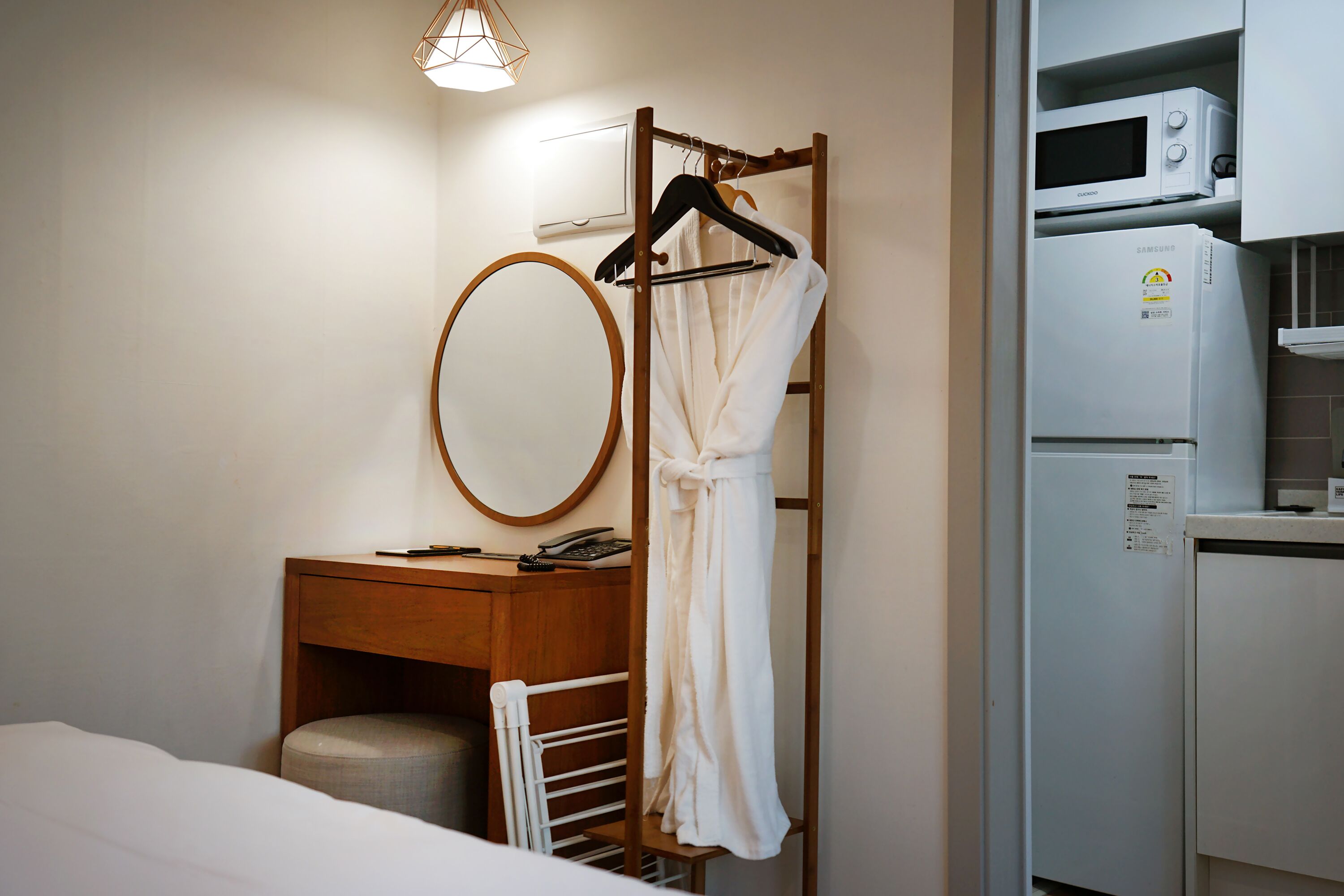 Quarto de hotel com uma cama, mesa de cabeceira de madeira com espelho, roupão pendurado em um suporte, radiador branco e micro-ondas.