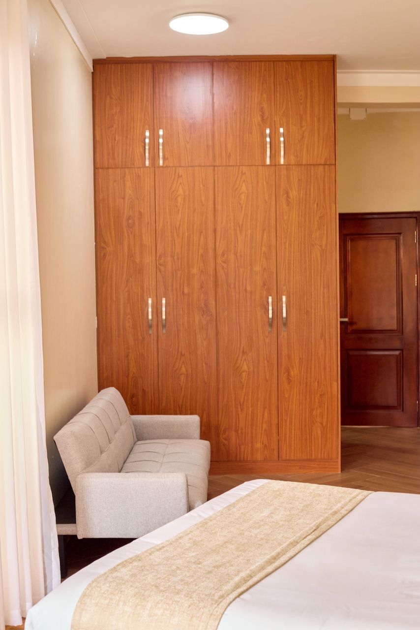 A bedroom with a large wooden wardrobe, a beige armchair, and a bed with a beige throw.