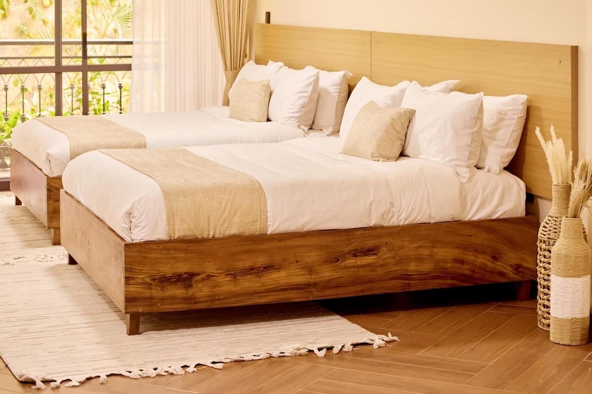 A bedroom with a large bed, a wooden headboard, a window with curtains, and a painting on the wall.
