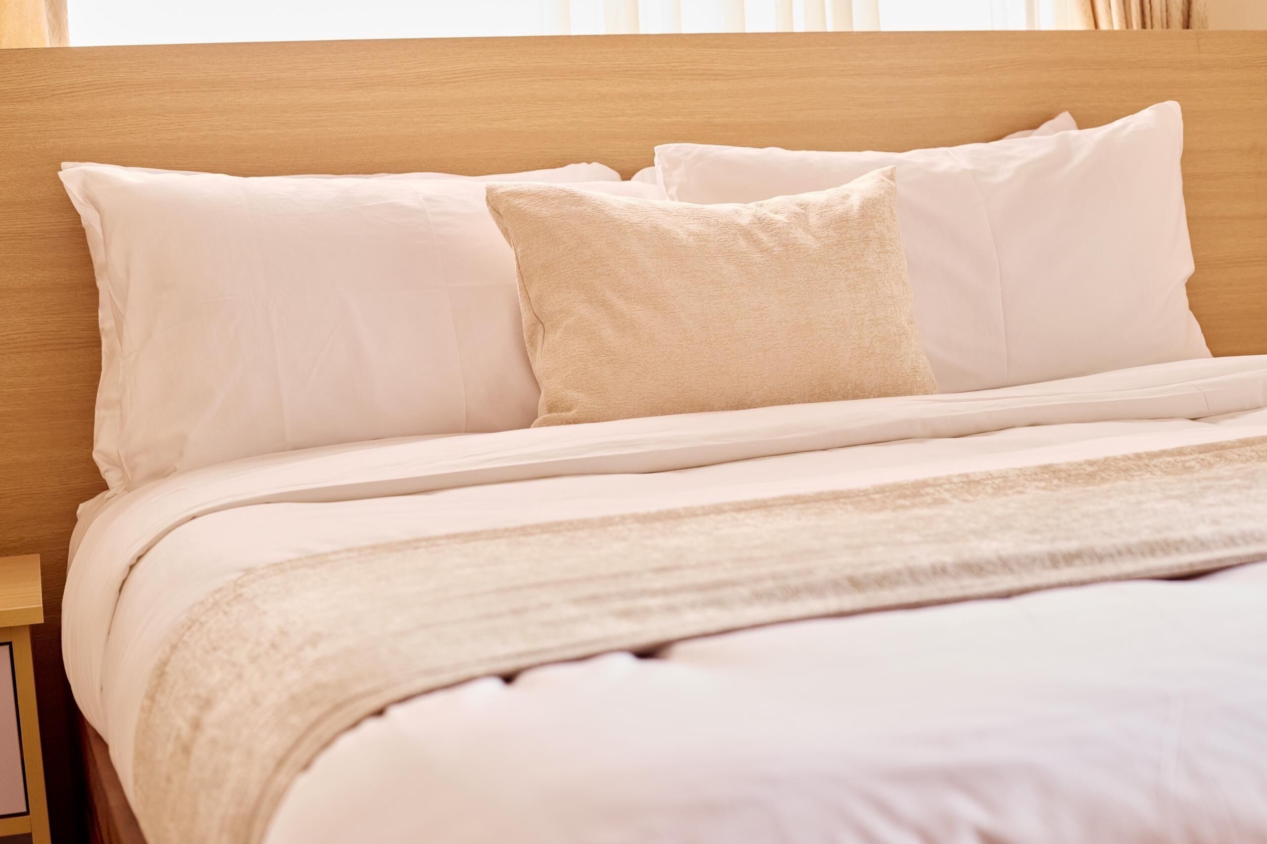 Una cama bien hecha con sábanas blancas y cabecera de madera.