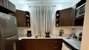 Una cucina compatta con mobili in legno, un frigorifero, un lavandino e un piccolo sgabello.