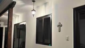 Un corridoio con pavimento piastrellato, un punto luce a parete e una porta decorata con una croce.