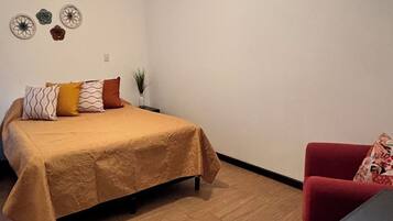 Een slaapkamer met een bed, een bureau, een rode stoel, een plafondventilator en een raam.