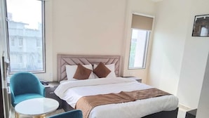A hotel room with a bed, two blue chairs, a small round table, and a window. - Hotel Fortune Elevate (Jaipur)