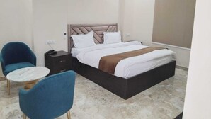 A bedroom with a bed, two chairs, a small table, and a nightstand. - Hotel Fortune Elevate (Jaipur)