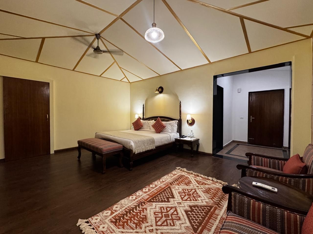 A bedroom with a bed, bedside tables, a bench, a patterned rug, and a door leading to another room.