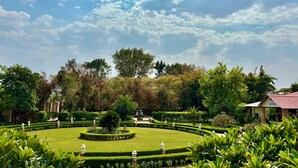 Een goed onderhouden tuin met een rond gazon, diverse planten en een gebouw met een rood dak.
