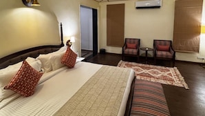 Een hotelkamer met een groot bed, een kleiner bed, een plafondventilator, een bureau met twee stoelen en een raam met jaloezieën.