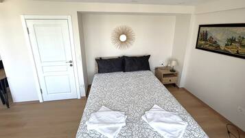 Een slaapkamer met een bed, nachtkastje, een spiegel aan de muur en een schilderij.