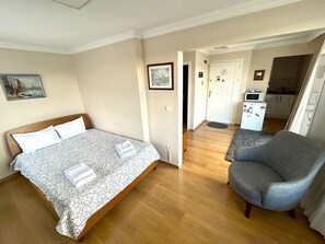 A hotel room with a bed, a grey armchair, a small kitchenette, and a door leading to another room. - Kuzguncuk View (Istanbul)