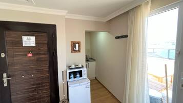 A hotel room with a wooden door, a small kitchenette, a microwave, and a view of the balcony.