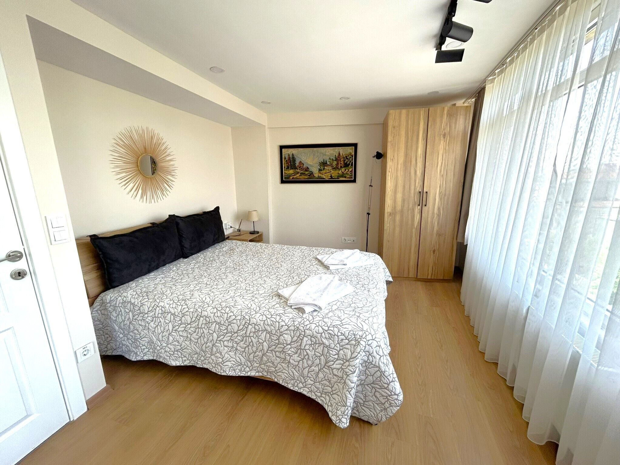 Un dormitorio con cama, armario, cuadro y espejo con efecto sol.